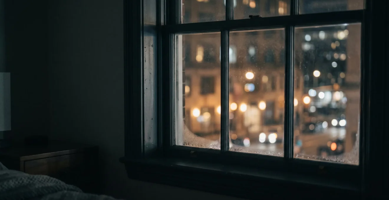 Vue nocturne d'une fenêtre de chambre avec lumière urbaine diffuse à travers le vitrage