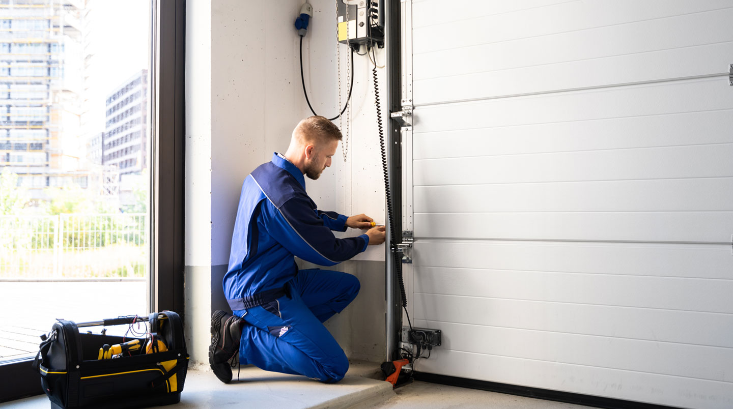 Technicien installateur professionnel ajustant les rails latéraux d'une porte de garage sectionnelle à l'intérieur d'un garage résidentiel, outils professionnels au premier plan