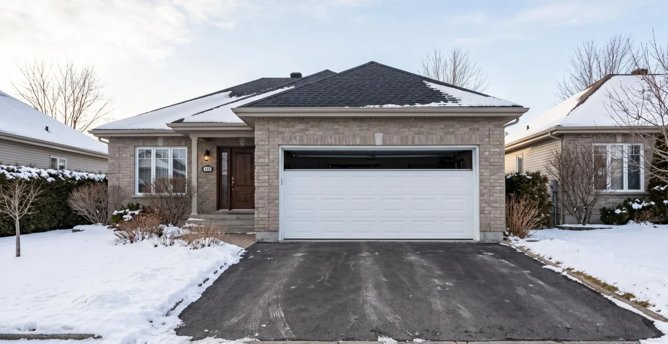Façade de bungalow résidentiel québécois avec porte de garage sectionnelle blanche double largeur installée, allée asphaltée dégagée, architecture typique Rive-Sud Montréal sous ciel d'hiver lumineux
